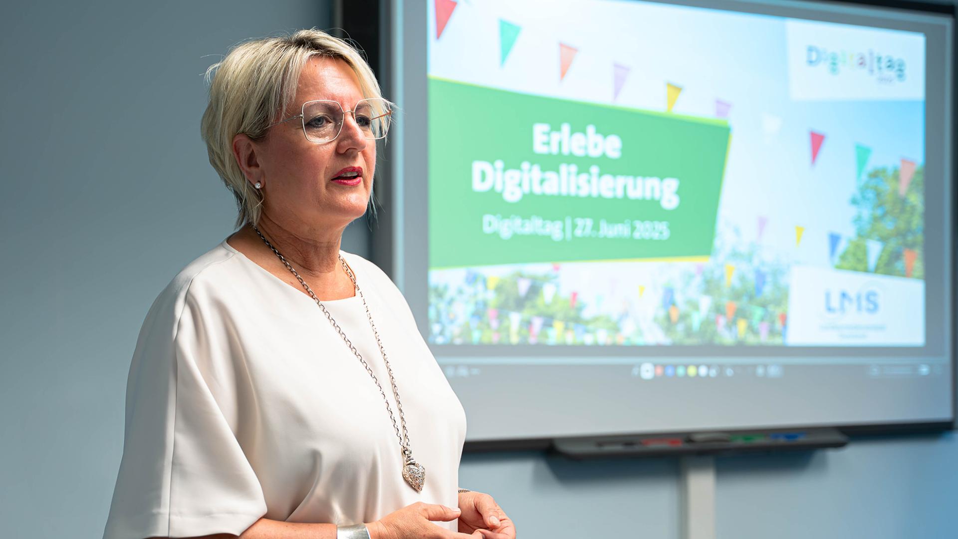 Direktorin Ruth Meyer vor einem Bildschirm mit der Aufschrift Erlebe Digitalisierung