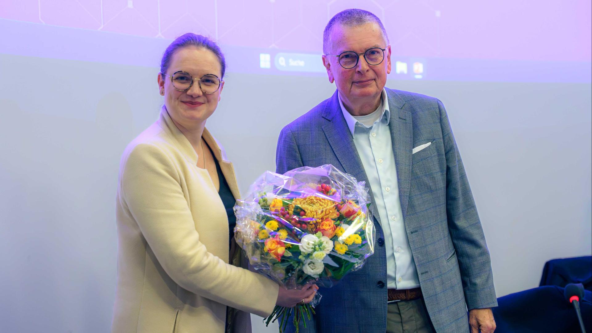 Julia Katharina Eßwein und Prof. Dr. Ory stehen nebeneinander und halten gemeinsam einen bunten Blumenstrauß in den Händen.