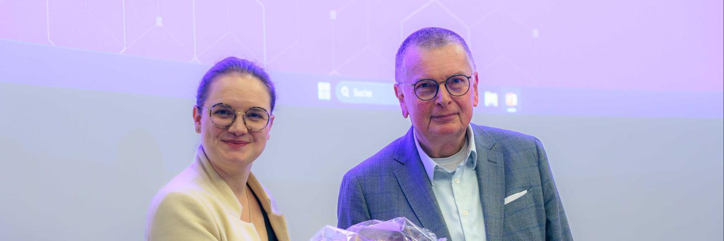 Julia Katharina Eßwein und Prof. Dr. Ory stehen nebeneinander und halten gemeinsam einen bunten Blumenstrauß in den Händen.